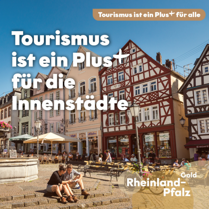 Belebter Platz mit historischen Fachwerkhäusern, Geschäften, Gastronomie und Außensitzplätzen bei blauem Himmel. Im Vordergrund sitzen zwei Personen am Brunnen. Darüber steht „Tourismus ist ein Plus+ für die Innenstädte“.